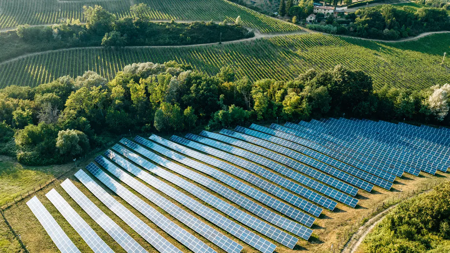 Aerial view of a solar energy farm with rows of solar panels installed across a rural landscape.
