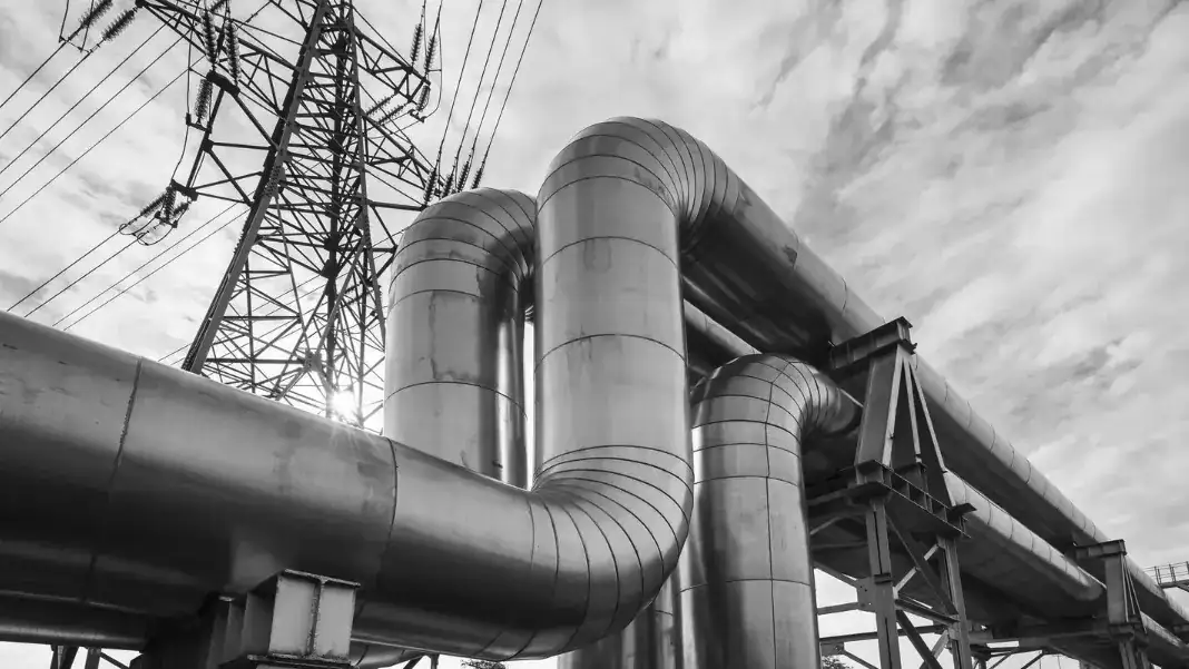 Large industrial piping and exhaust systems at an energy or manufacturing facility, shown with high-voltage power infrastructure.