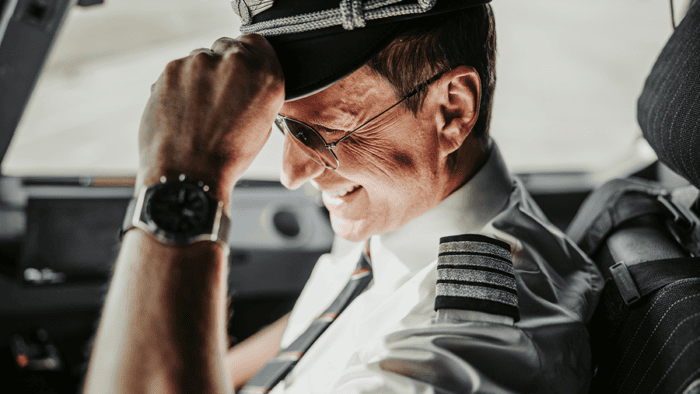 Pilot smiling in cockpit, wearing uniform.