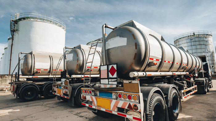 A line of commercial fleet vehicles parked next to industrial bulk fuel storage tanks