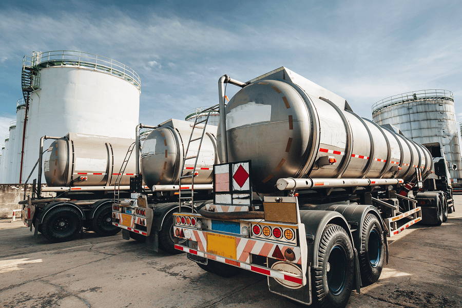 A line of commercial fleet vehicles parked next to industrial bulk fuel storage tanks