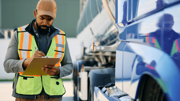 Man with clipboard and safety vest next to truck