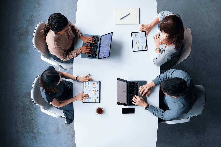 four people sitting at a table on their devices