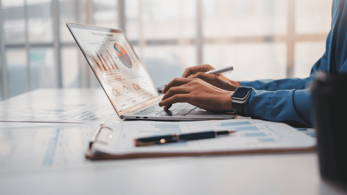 hands on a laptop while viewing a chart on screen