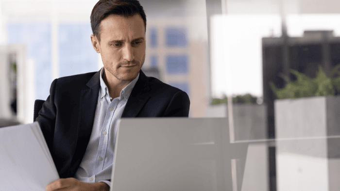 Businessman reviewing documents on laptop.