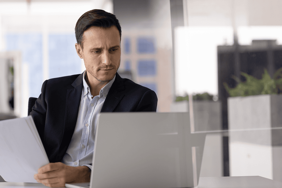Businessman reviewing documents on laptop.