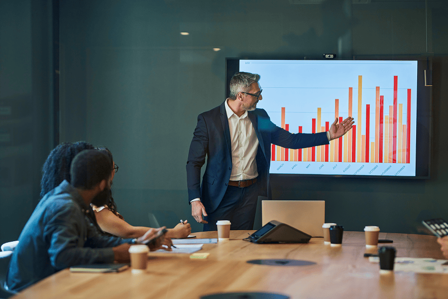 Business professional presenting performance metrics and bar charts to colleagues during a meeting.