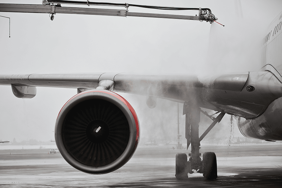 Commercial aircraft undergoing de-icing on an airport tarmac, with spray equipment applying fluid to the wing and engine area.
