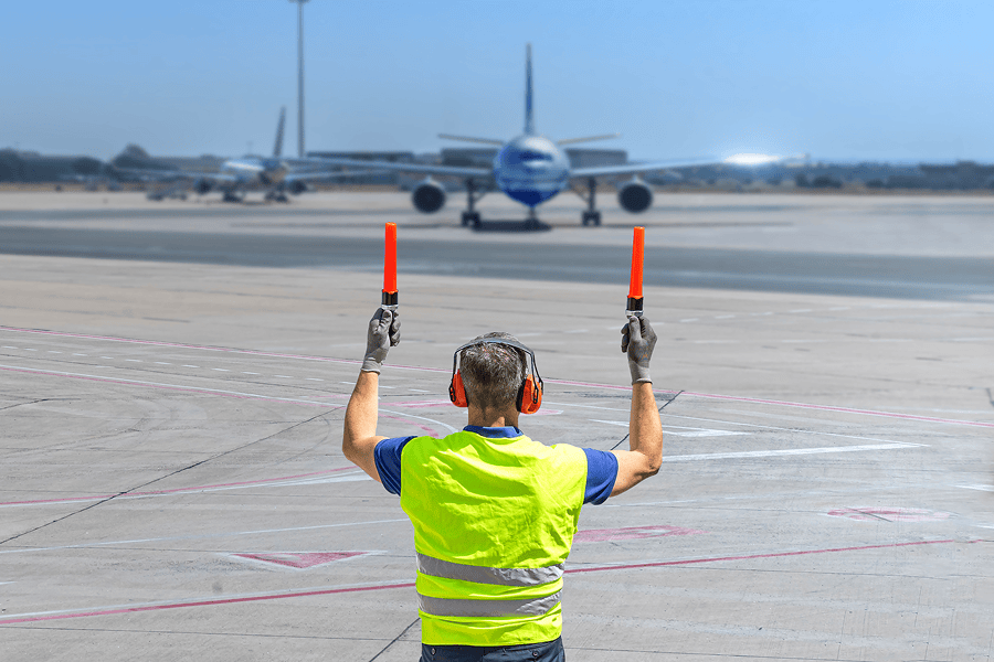 Airport ground crew member directing an aircraft on the tarmac using illuminated signal wands.