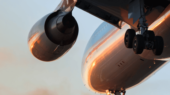 Close-up view of a commercial aircraft during flight or takeoff, showing the engine, landing gear, and underside of the fuselage.