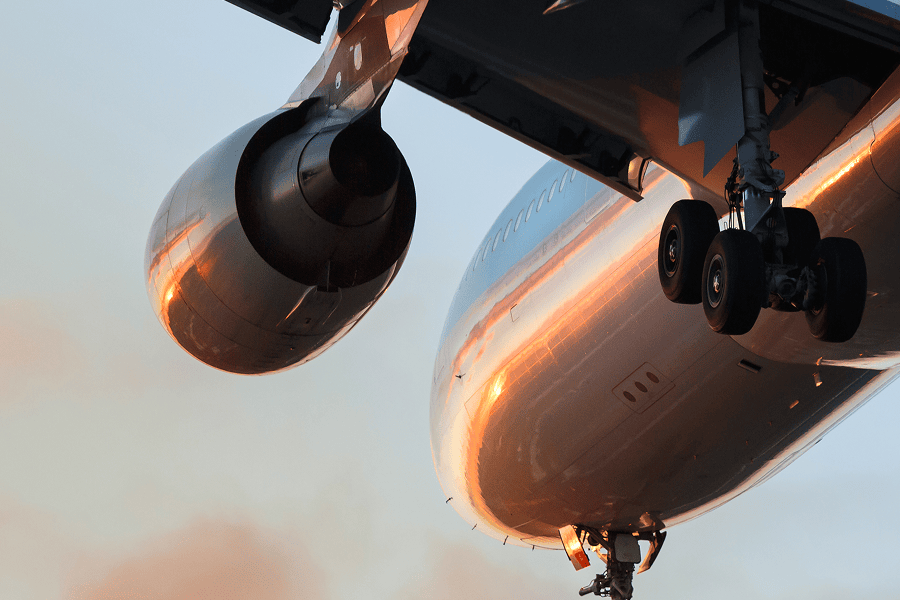 Close-up view of a commercial aircraft during flight or takeoff, showing the engine, landing gear, and underside of the fuselage.