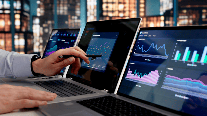 Business professional reviewing analytics dashboards and performance metrics across multiple laptop screens.
