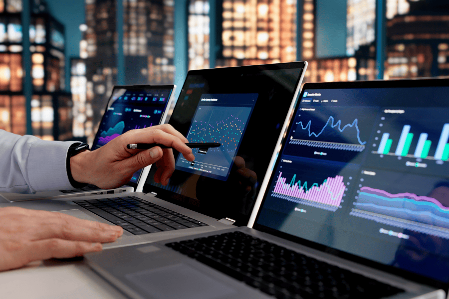 Business professional reviewing analytics dashboards and performance metrics across multiple laptop screens.