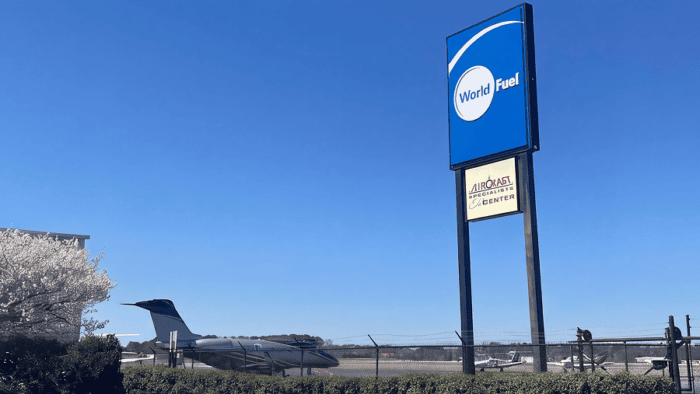 World Fuel aviation facility sign displayed near an airport runway with aircraft visible in the background.