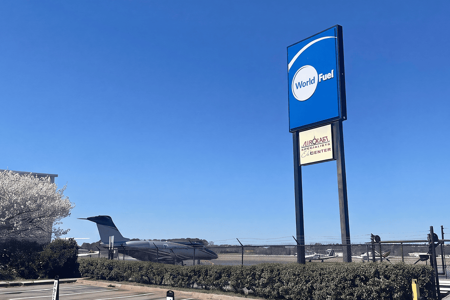 World Fuel aviation facility sign displayed near an airport runway with aircraft visible in the background.