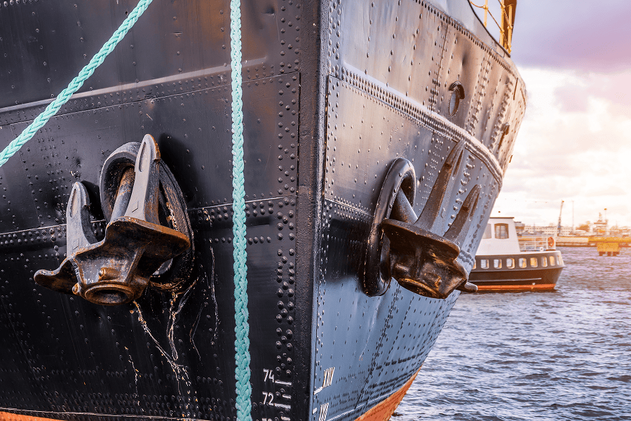 Close-up view of a ship’s bow with two anchors secured to the hull while docked near a harbor.