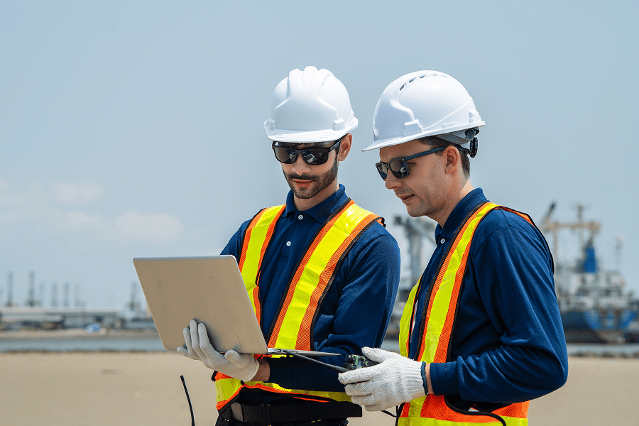 A team of maritime industrial engineers and field specialists discussing site logistics next to heavy infrastructure at a commercial terminal.