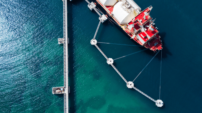 Aerial view of an LNG carrier docked at an offshore terminal, connected to a network of loading platforms and mooring structures.