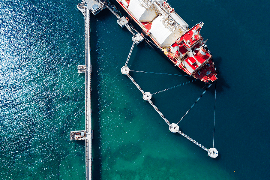 Aerial view of an LNG carrier docked at an offshore terminal, connected to a network of loading platforms and mooring structures.