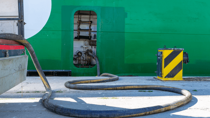 A fuel pipe connected to an industrial tanker vessel during bunker refueling operations at a port