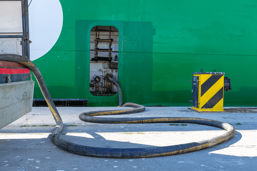 A fuel pipe connected to an industrial tanker vessel during bunker refueling operations at a port