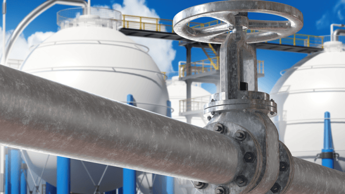 Industrial gas storage facility with a large pipeline valve in the foreground and multiple storage tanks in the background.