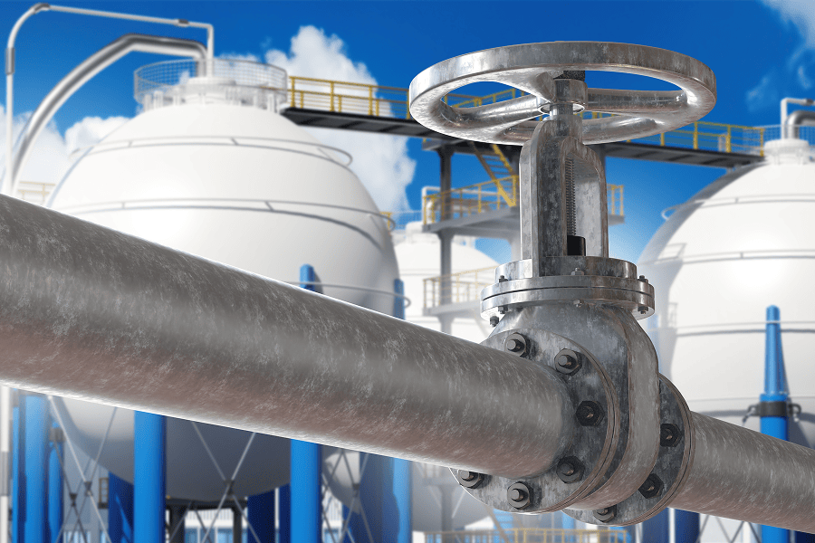 Industrial gas storage facility with a large pipeline valve in the foreground and multiple storage tanks in the background.