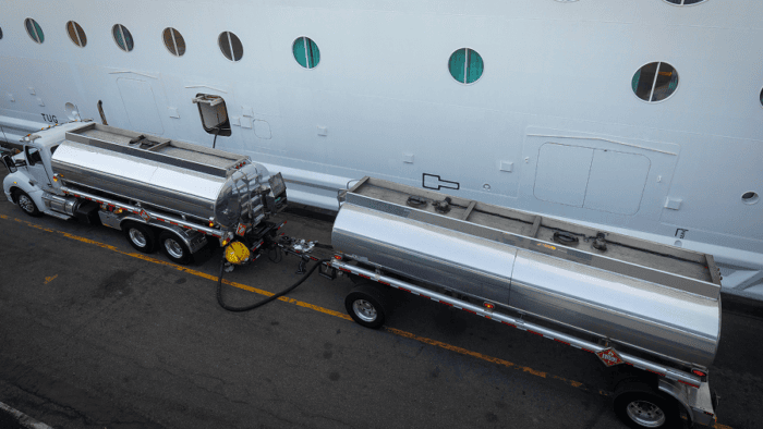 A commercial fuel tanker truck refueling a cruise ship at a passenger port terminal
