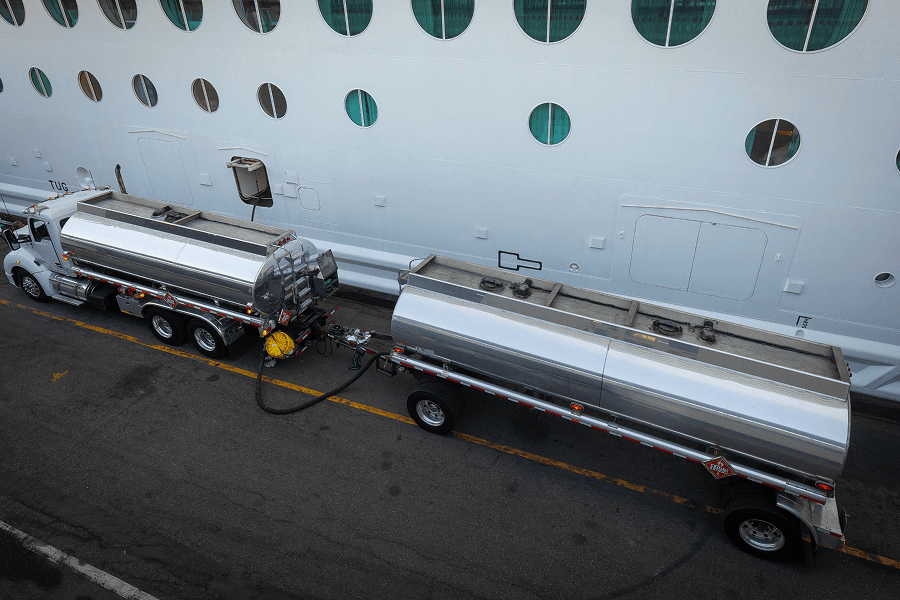 A commercial fuel tanker truck refueling a cruise ship at a passenger port terminal