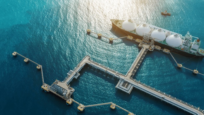 Aerial view of a liquefied natural gas (LNG) carrier docked at an offshore terminal connected by pipelines and loading infrastructure.