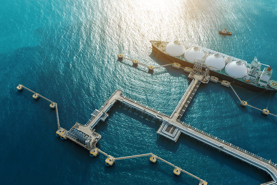 Aerial view of a liquefied natural gas (LNG) carrier docked at an offshore terminal connected by pipelines and loading infrastructure.