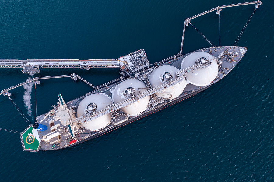 Aerial view of an LNG carrier docked at a marine terminal, connected to loading infrastructure extending into the water.