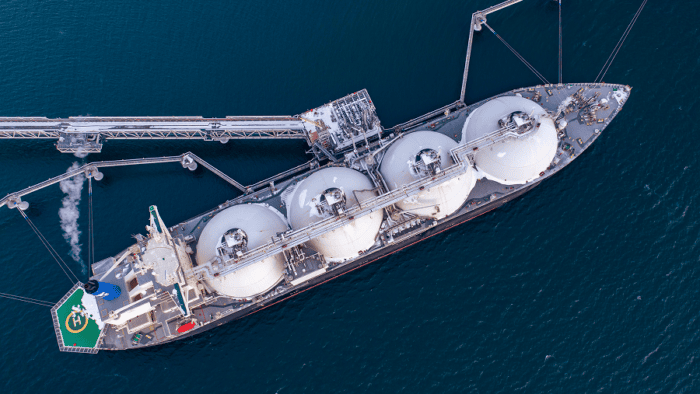 Aerial view of an LNG carrier docked at a marine terminal, connected to loading infrastructure extending into the water.