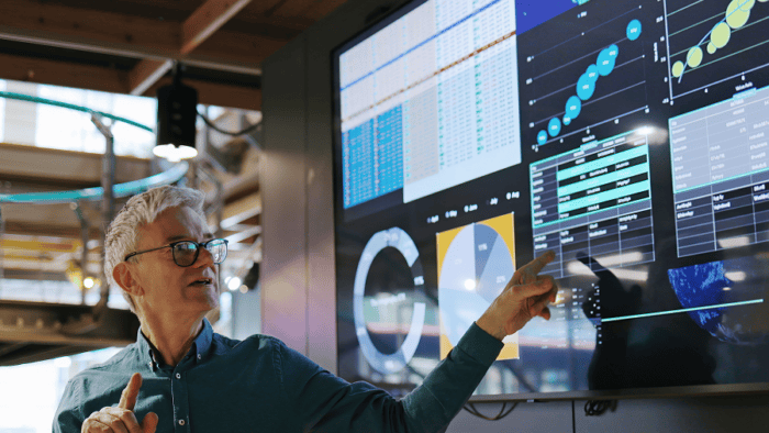A close-up of a male analyst pointing at data graphs and metrics on a computer monitor