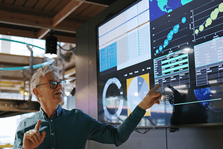 A close-up of a male analyst pointing at data graphs and metrics on a computer monitor