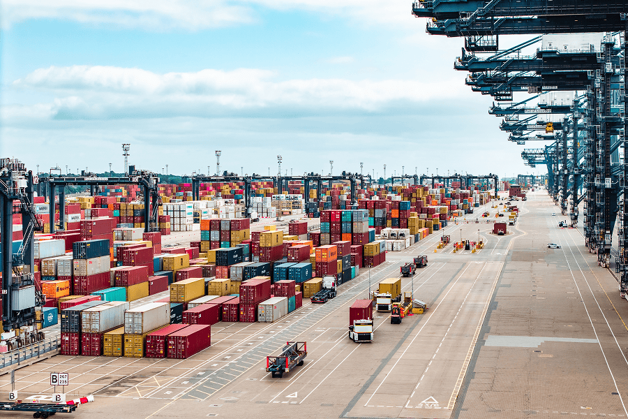 Busy container terminal with stacks of shipping containers, cargo handling equipment, and transport vehicles.