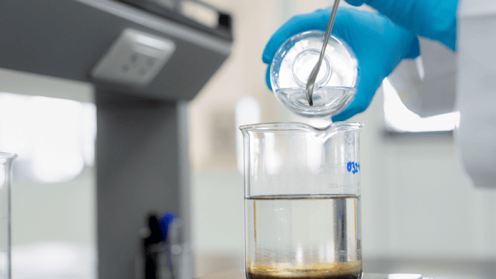 A laboratory technician analyzing an oil sample inside a glass beaker