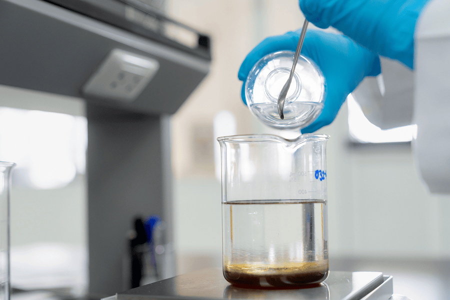 A laboratory technician analyzing an oil sample inside a glass beaker