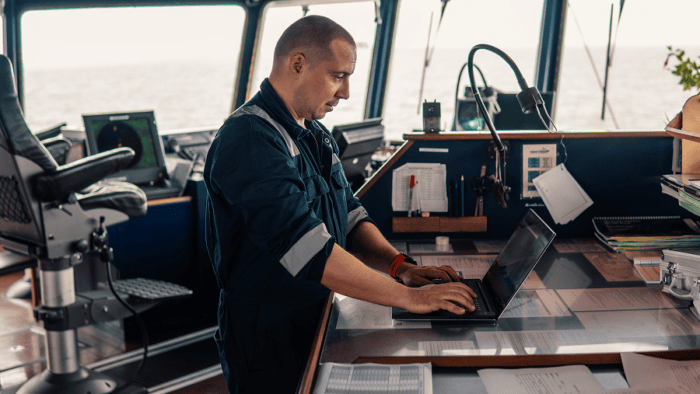 A maritime ship officer using a laptop inside the bridge control room