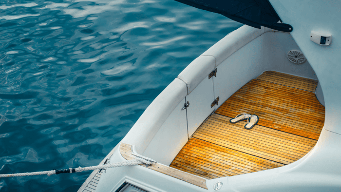 Luxury yacht stern with a teak deck and a pair of sandals resting beside calm blue water.