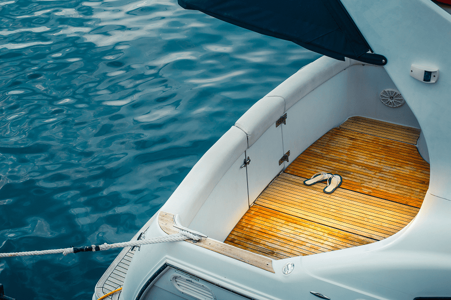 Luxury yacht stern with a teak deck and a pair of sandals resting beside calm blue water.