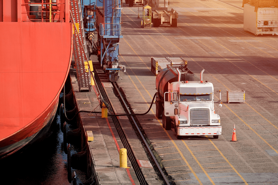 A fuel truck refueling a maritime vessel at a port terminal