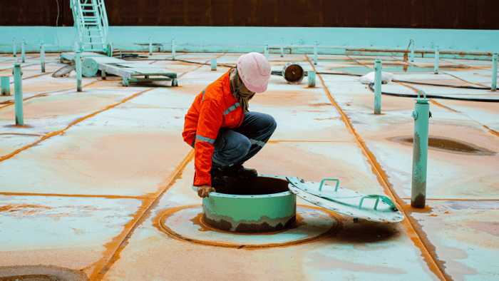 A maritime logistics worker walking across the fuel tanker surface to conduct an inspection