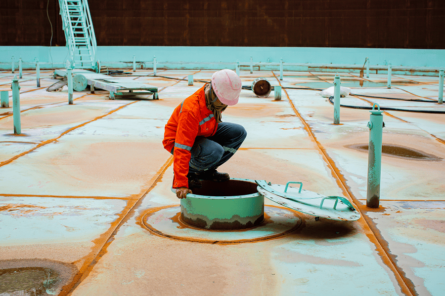 A maritime logistics worker walking across the fuel tanker surface to conduct an inspection