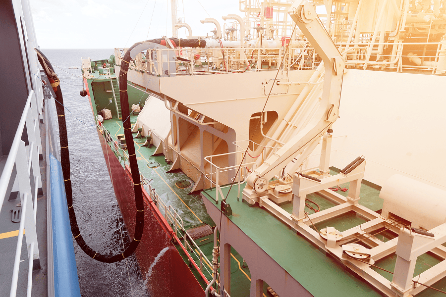 A marine ship refueling connection showing a flexible hose delivering fuel to a commercial vessel at dock