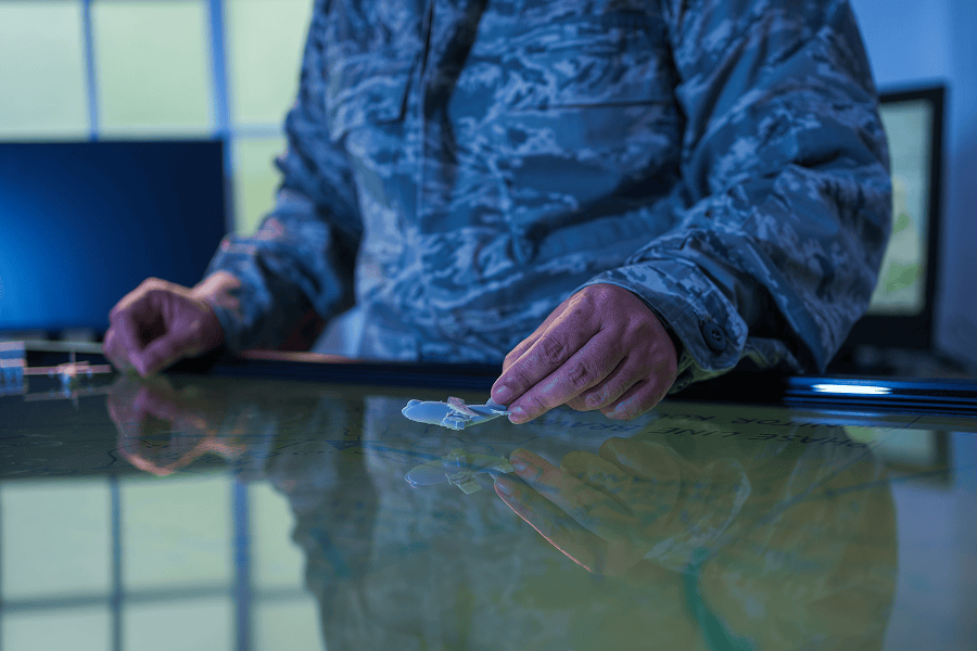 A military man moves a marker across a large digital map table