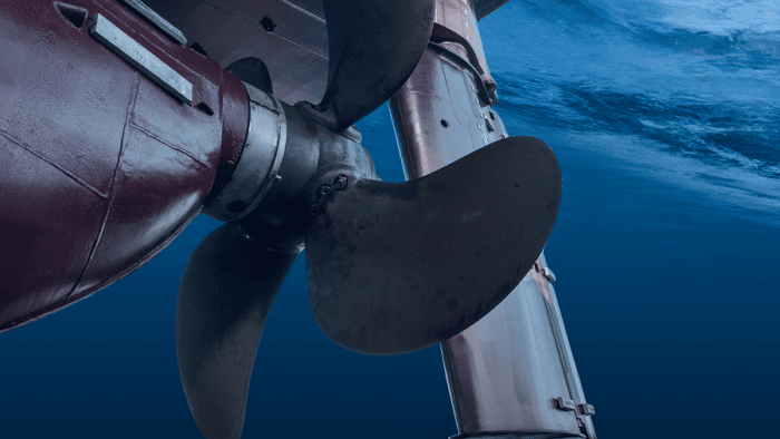 Close-up view of a ship’s propeller and rudder partially submerged in blue ocean water.