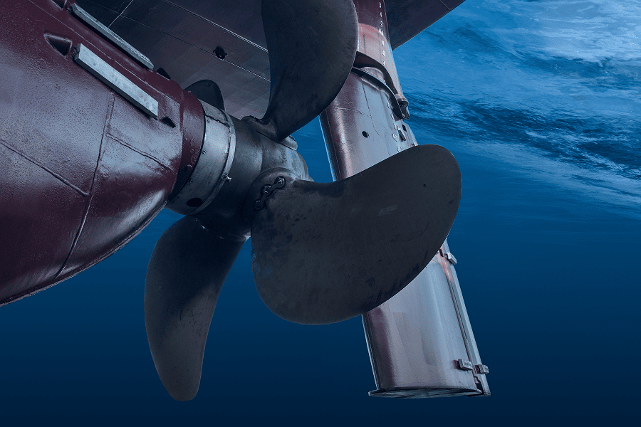 Close-up view of a ship’s propeller and rudder partially submerged in blue ocean water.