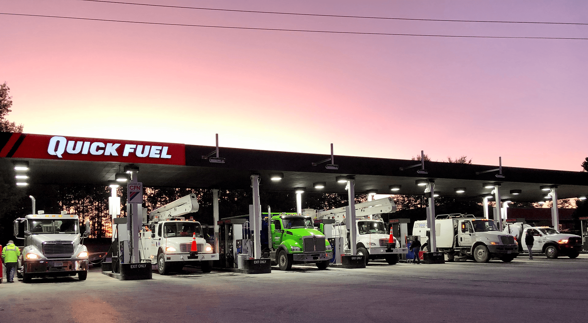 A commercial fleet vehicle refueling at a Quickfuel cardlock fuel station during a clear sunset