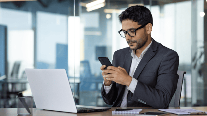 Businessman focused on phone at desk.